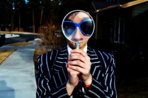 A face in sunglasses looking through a magnifying glass.