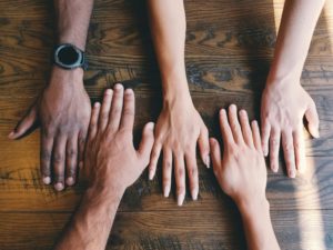 Five hands meeting on an old wood table.